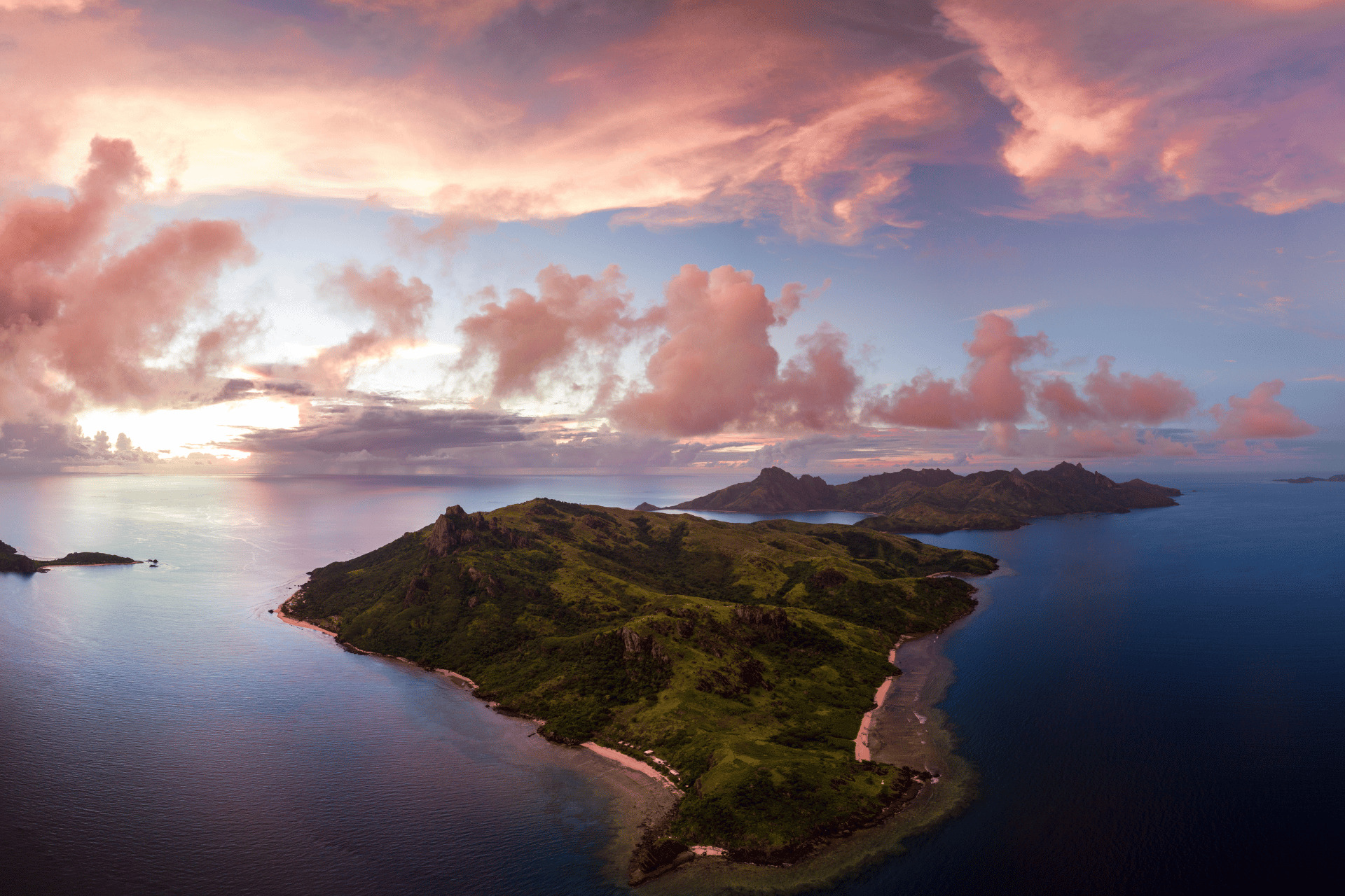 An aerial view of the island of Fiji with pink clouds.