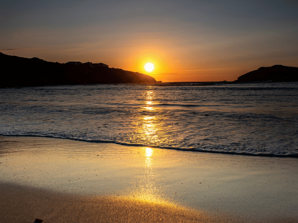 The sun is setting over the beach in Newquay Cornwall UK. 