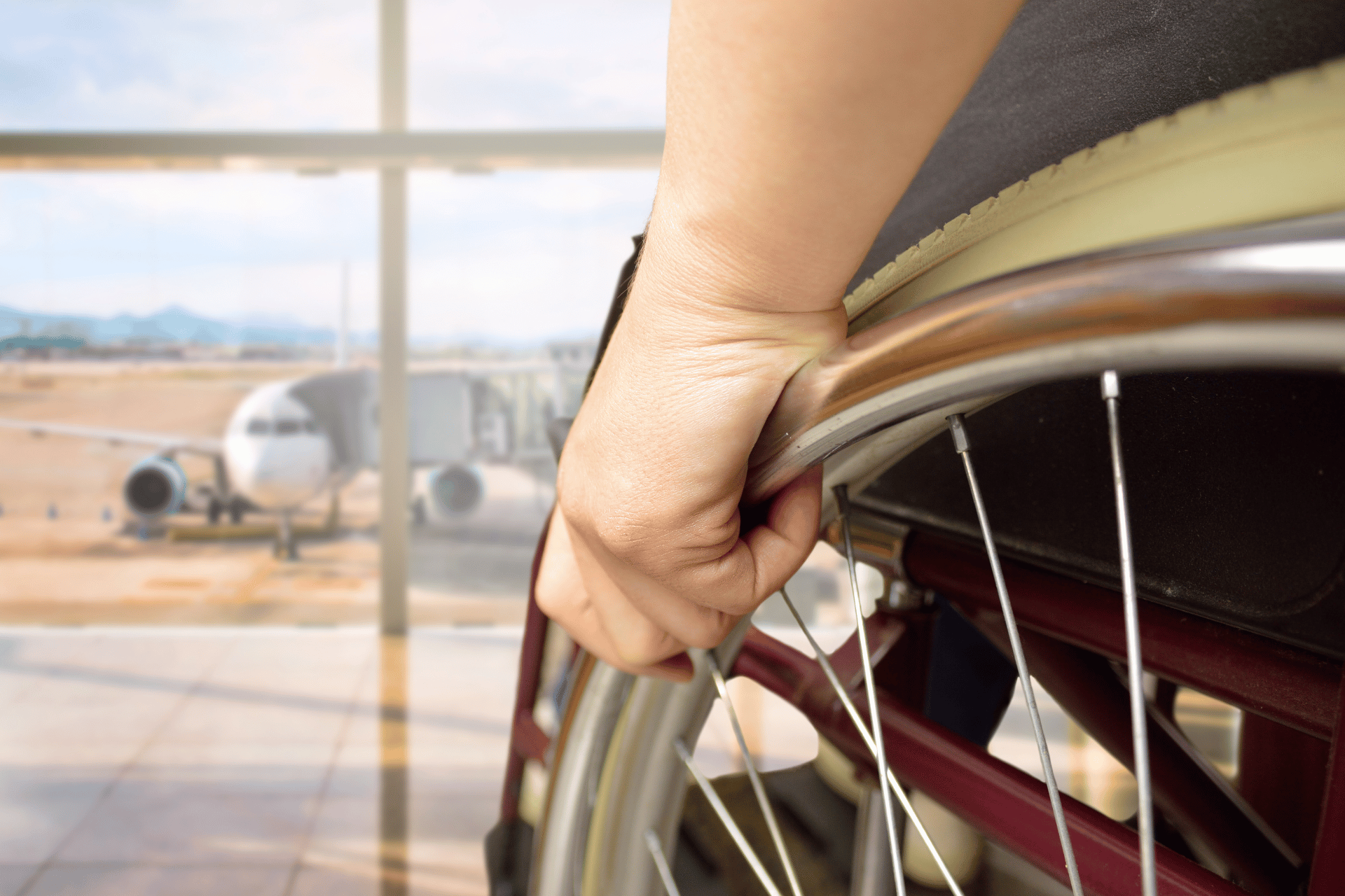 A plane in the background of an airport with a man in a wheelchair looking out