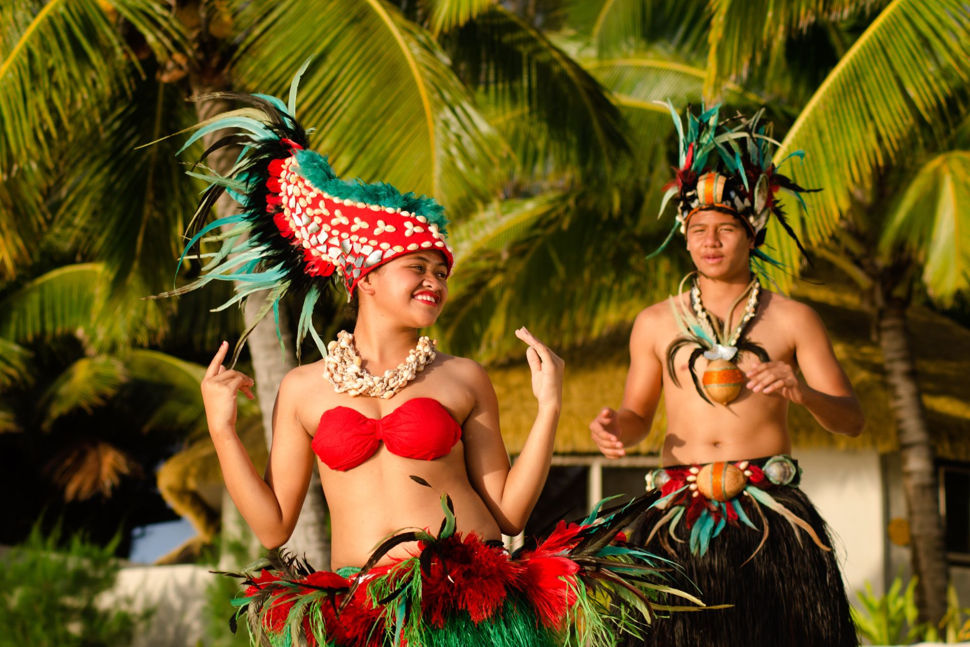 Portrait of attractive young Polynesian Pacific Island Tahitian male and female dancers in colorful costumes dancing on tropical beach during sunset with palm trees in the background. ©Getty Images