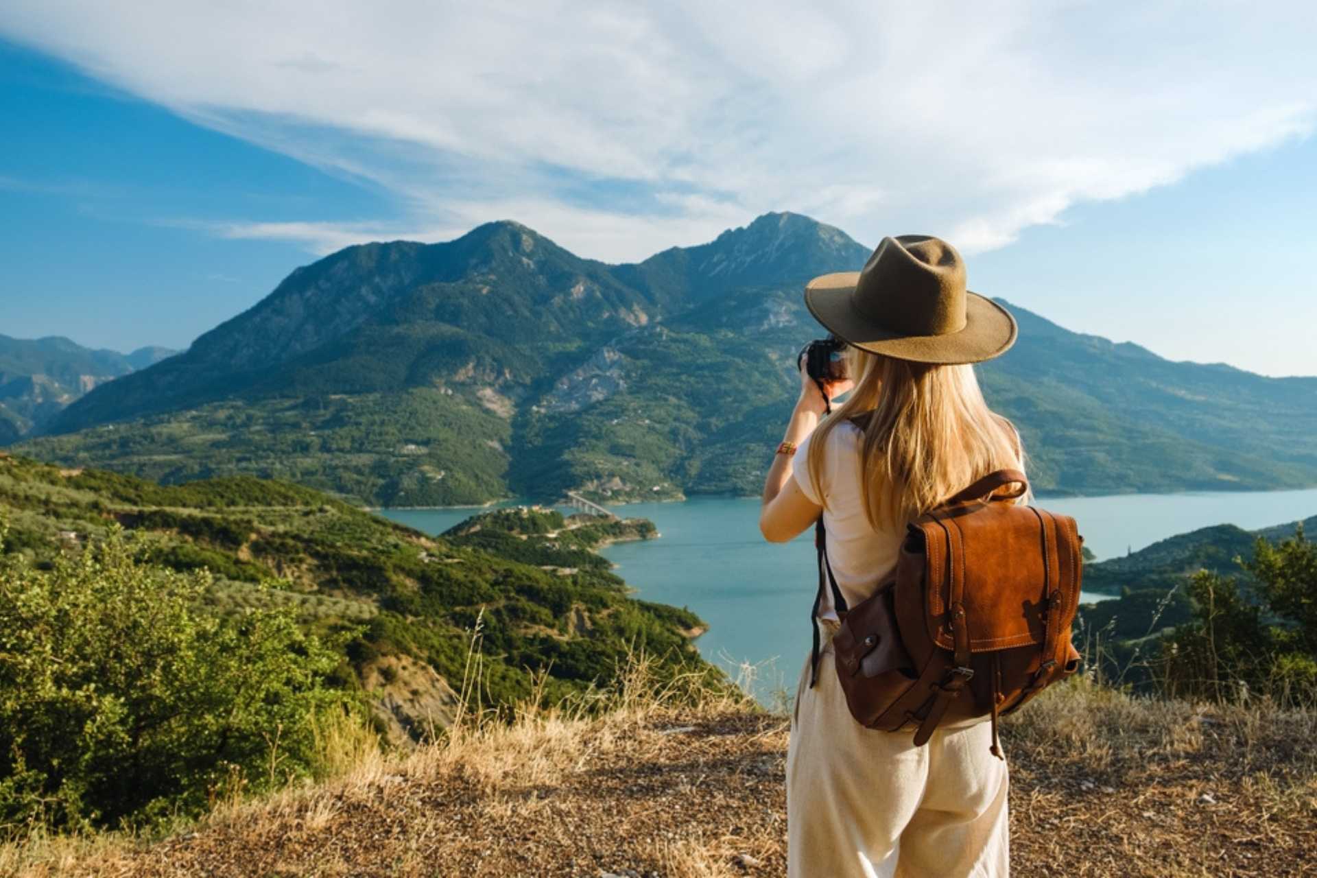 Woman photographer with big backpack taking photo of mountains and blue lake. Travel and hobby concept