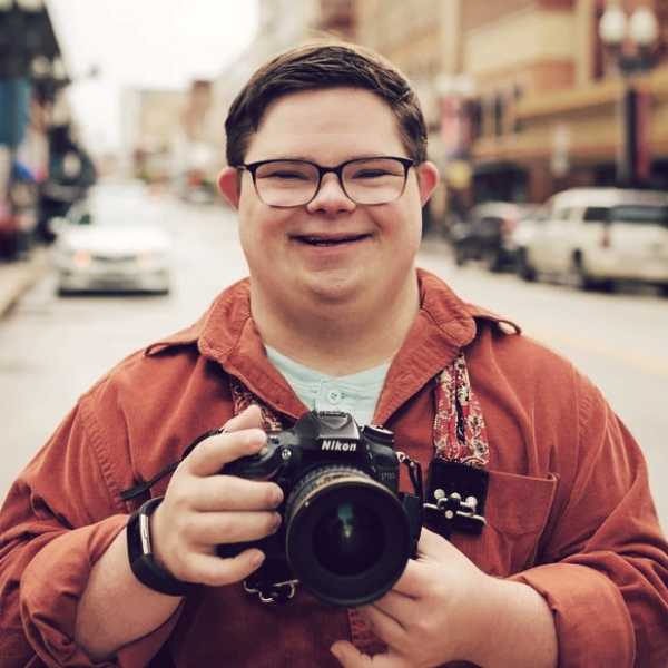 Houston Vandergriff, Photographer. Houston is smiling into the camera holding his Nikon camera.