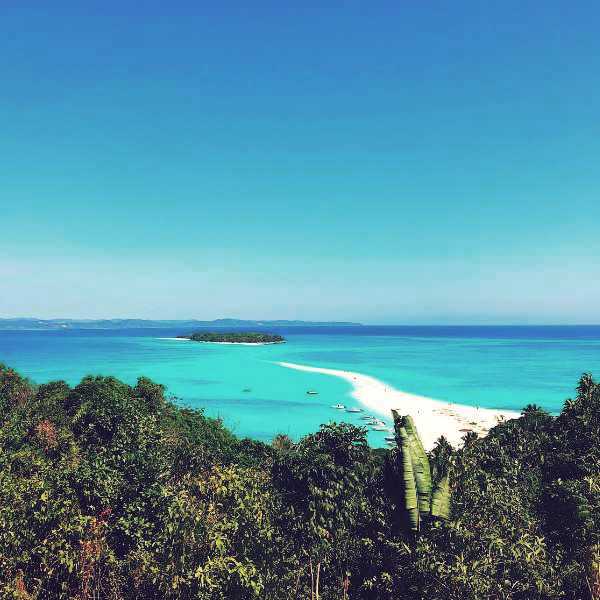 Turquoise waters and white sandy beach of Nosy Iranja Nosy Be Madagascar. viewed from a lush tropical hillside.