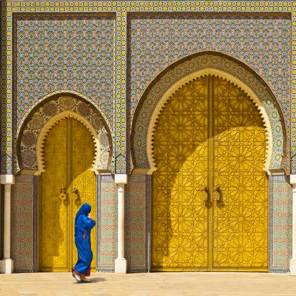 A person wearing a blue robe walks in front of a golden door in Fes, door of Royal palace.Getty Images