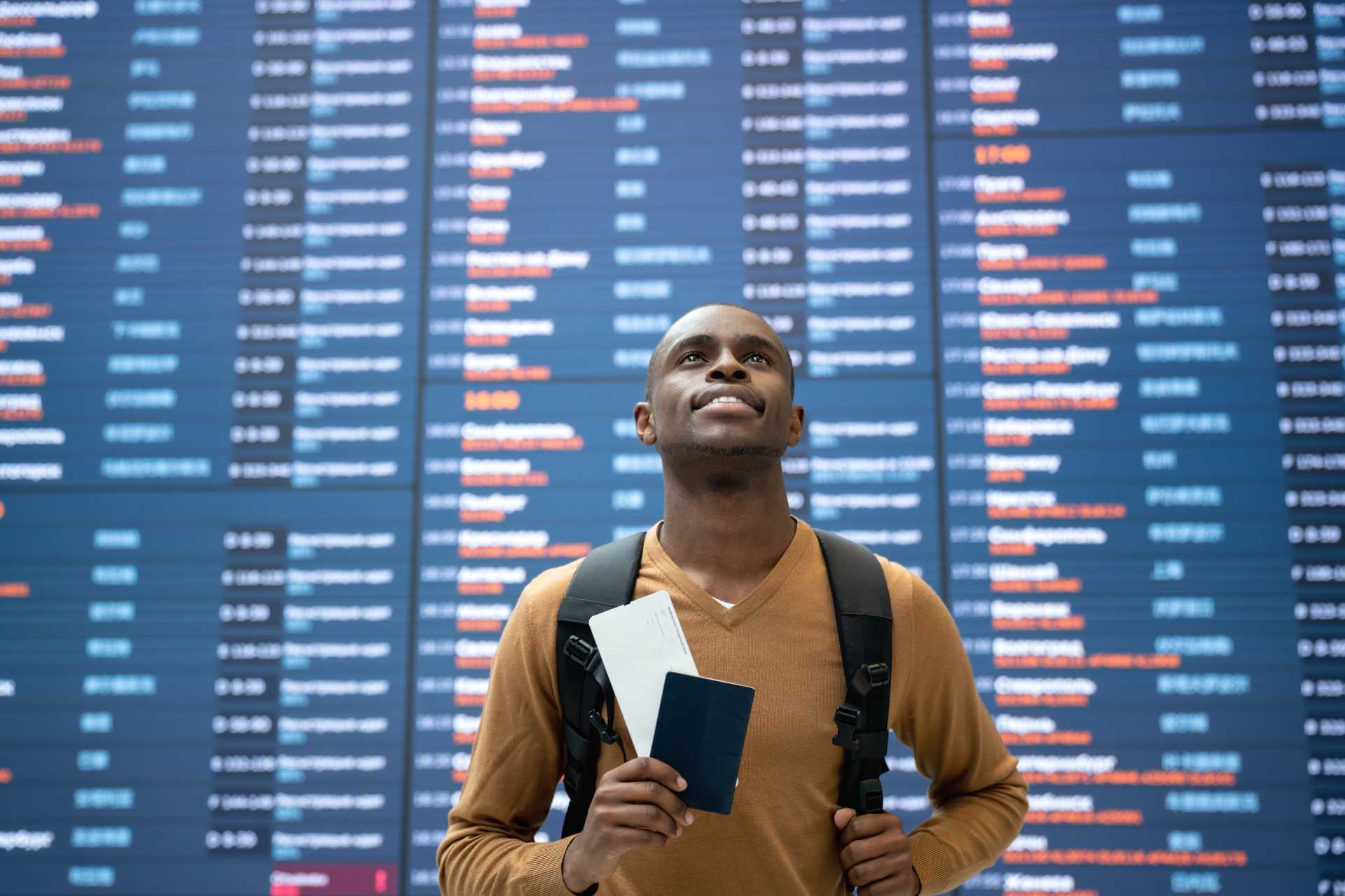 Portrait of a happy black male traveler at the airport with the flight schedule at the background and holding his passport - travel concepts©Getty Images
